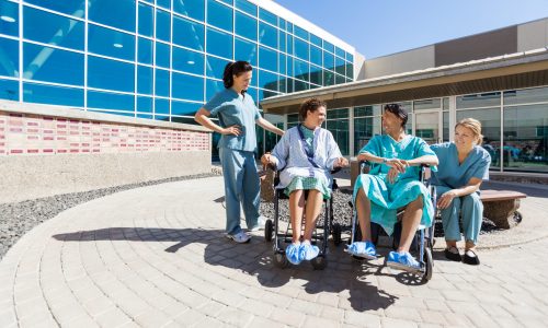 Male and female patients on wheelchair looking at each other by nurses outside hospital building